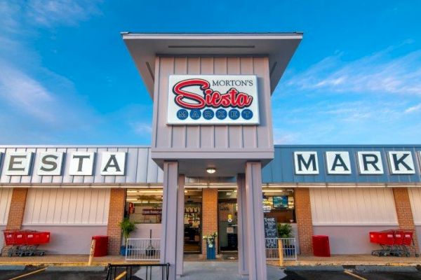 The image shows the front of Morton's Siesta Market with shopping carts and a clear blue sky, emphasizing its inviting entrance and signage.