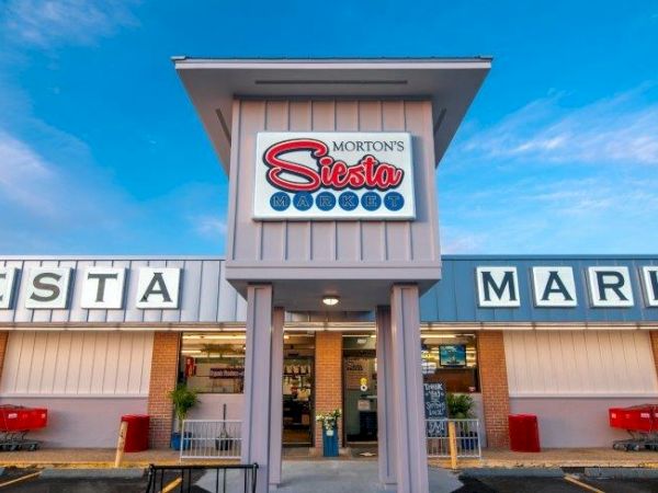 The image shows the front of Morton's Siesta Market with shopping carts and a clear blue sky, emphasizing its inviting entrance and signage.