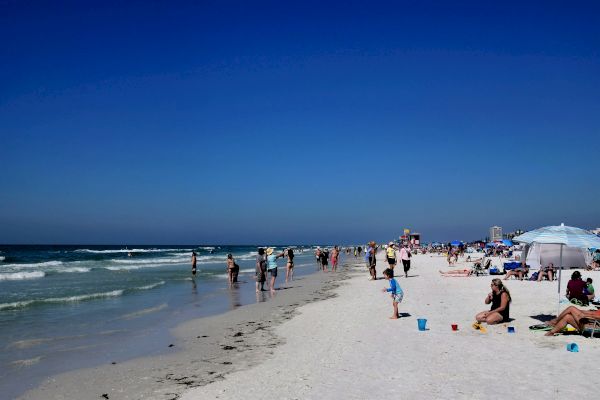 A crowded beach scene with people enjoying the sun, sand, and sea, with umbrellas and a clear blue sky.