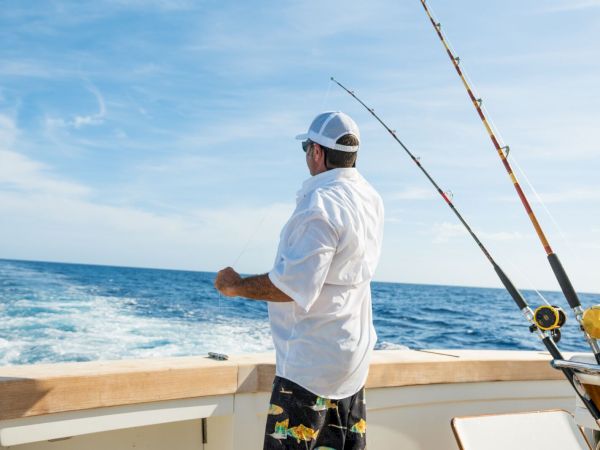 A person fishing at the back of a boat in the ocean, holding a line, with multiple fishing rods in view.