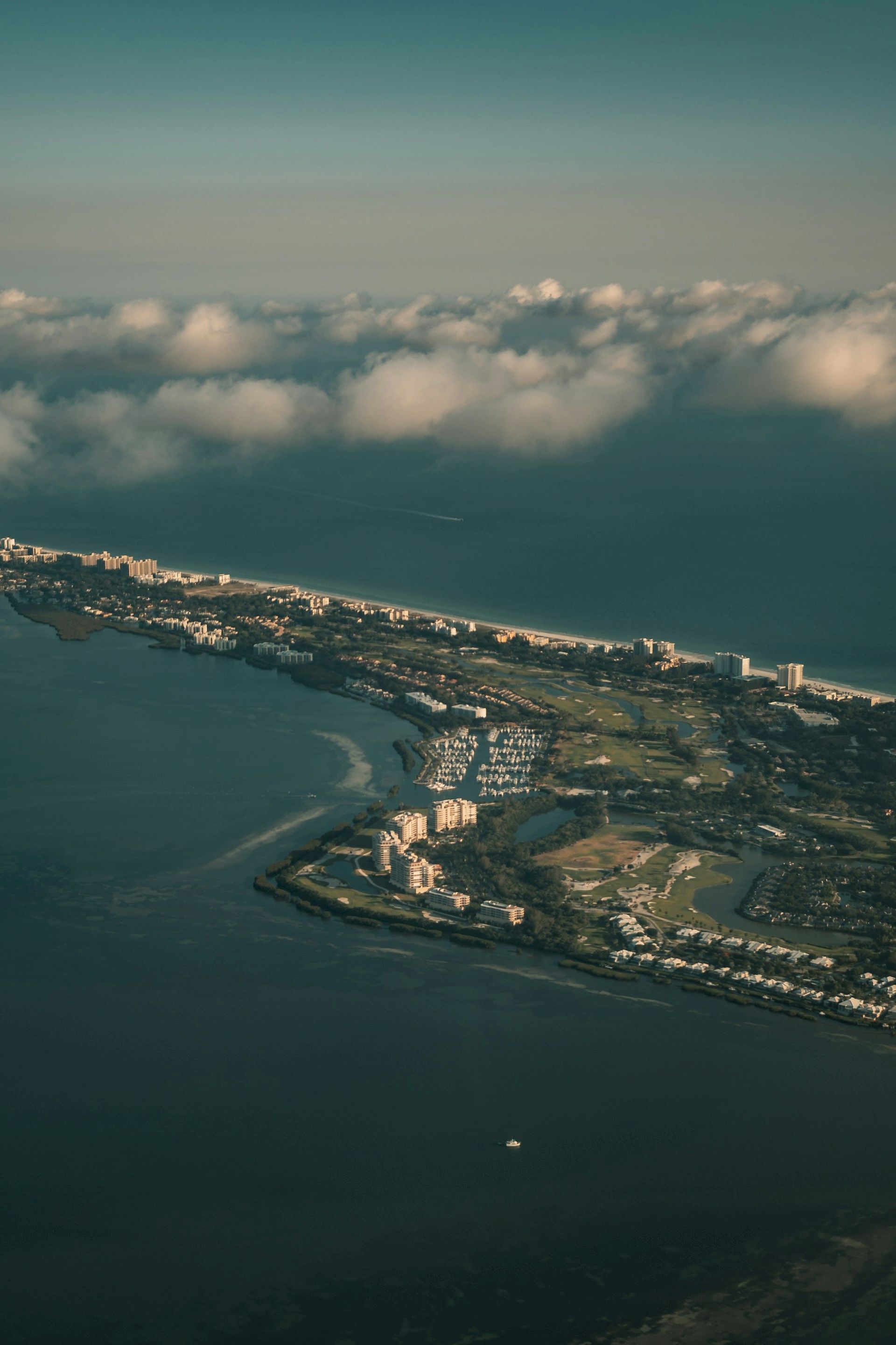 Aerial view of a coastal cityscape with clouds above, showing buildings, water, and land meeting the sea, with a serene atmosphere.