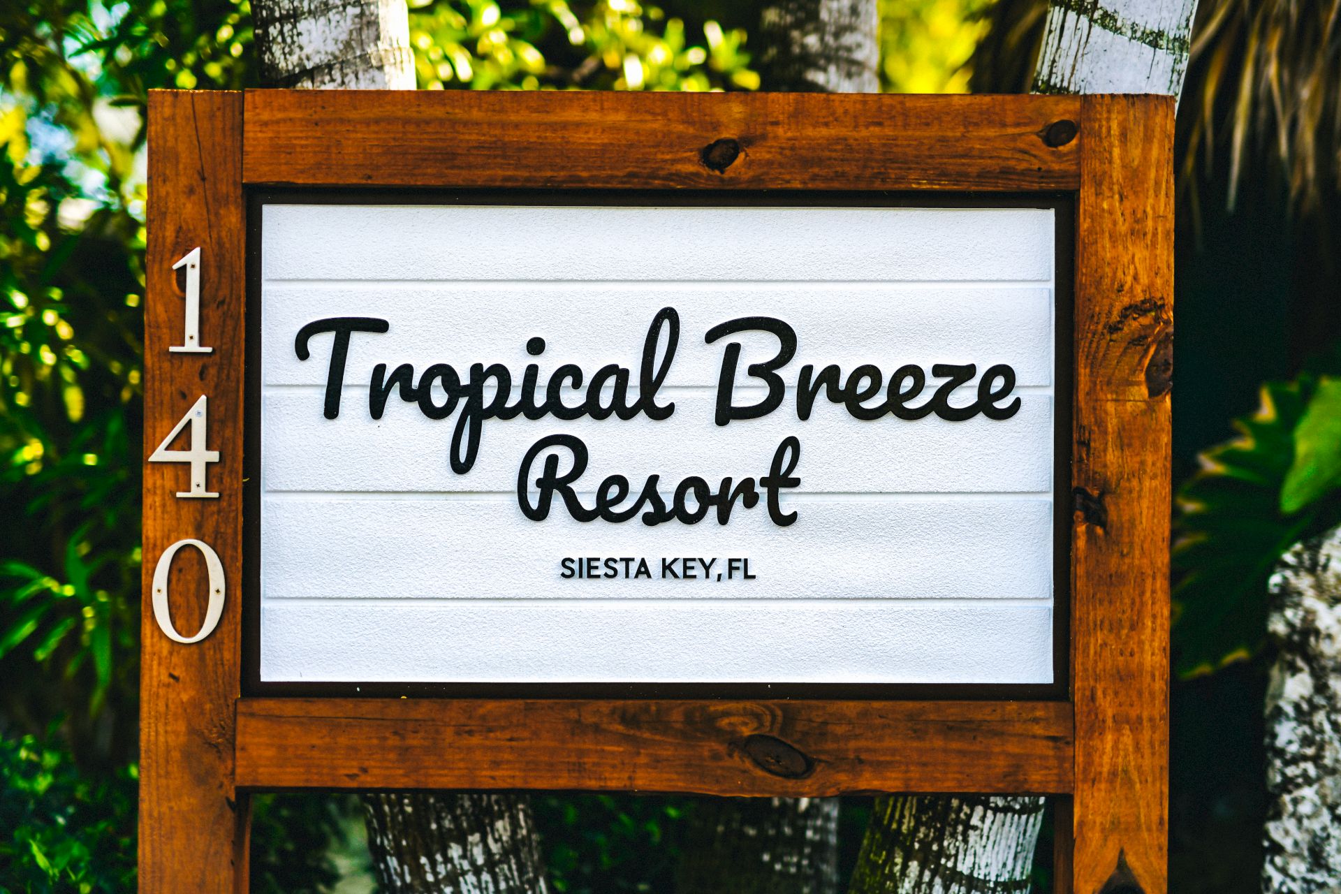 A wooden sign for "Tropical Breeze Resort" in Siesta Key, FL, surrounded by palm trees.