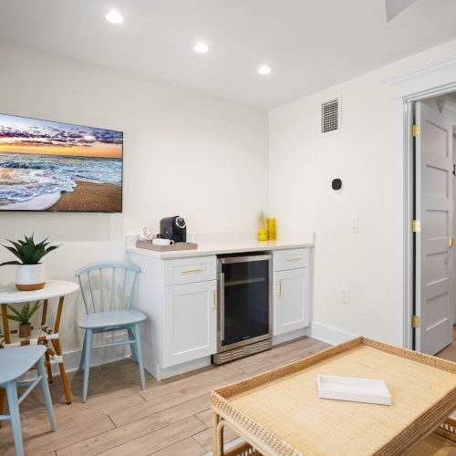 A cozy room with a TV, small table and chairs, cabinet with mini fridge, houseplant, and hallway in a light-toned aesthetic ends the sentence.