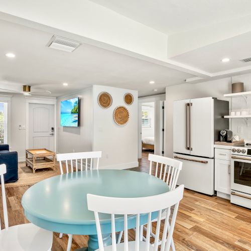 A modern, open-plan kitchen and living area with wooden floors, teal and white furniture, and decorative elements on the wall.