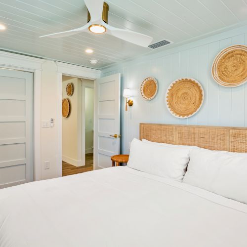 A cozy bedroom featuring a large bed, wicker wall decor, ceiling fan, and sliding closet doors, creating a serene ambiance.