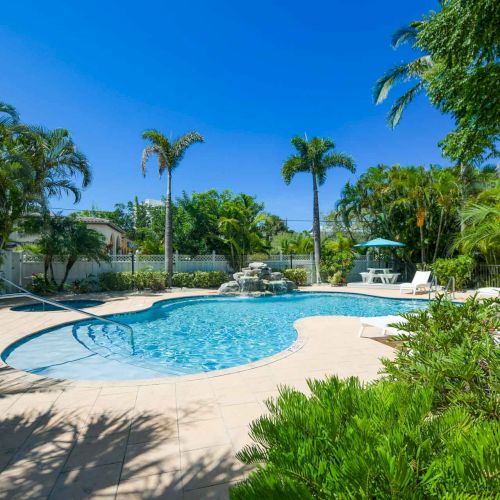 A serene outdoor pool area with palm trees, lounge chairs, and a sunny blue sky.