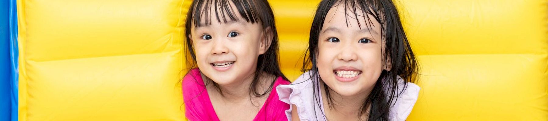 Two young children smiling inside a yellow inflatable structure, looking joyful in their colorful outfits.