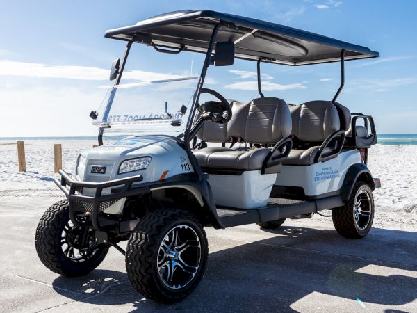 A covered, multi-seat off-road golf cart/utility vehicle parked on a sunny beach by the ocean, ready for rides.