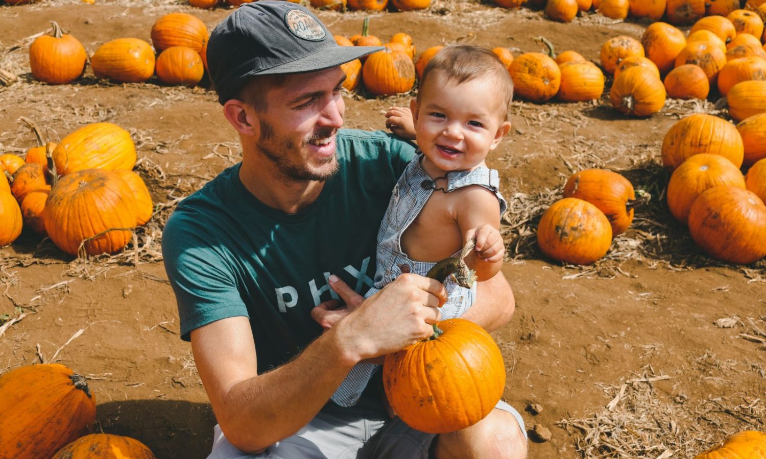 man holding baby in pumpkin patch
