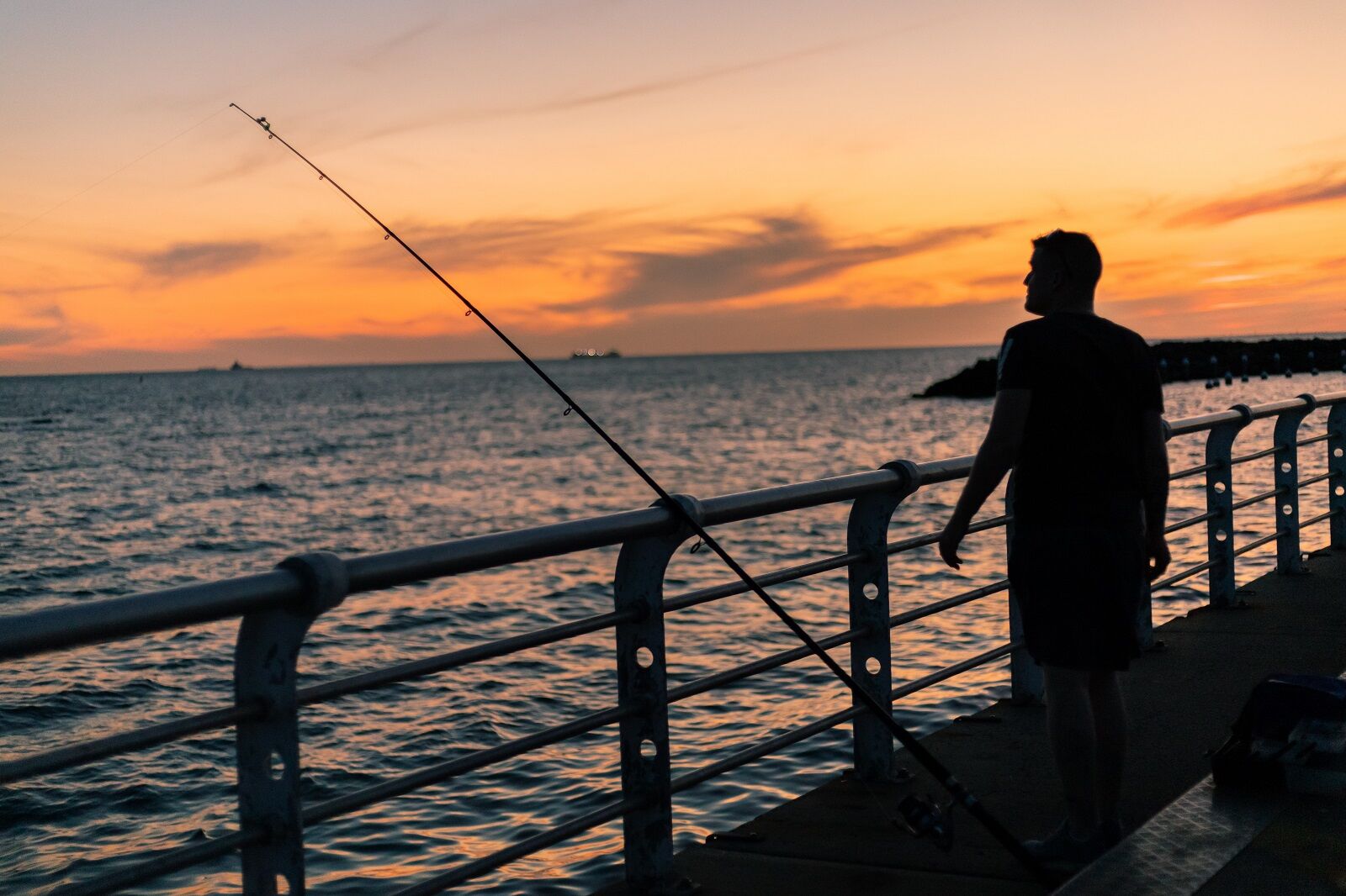 man fishing on a pier at sunset